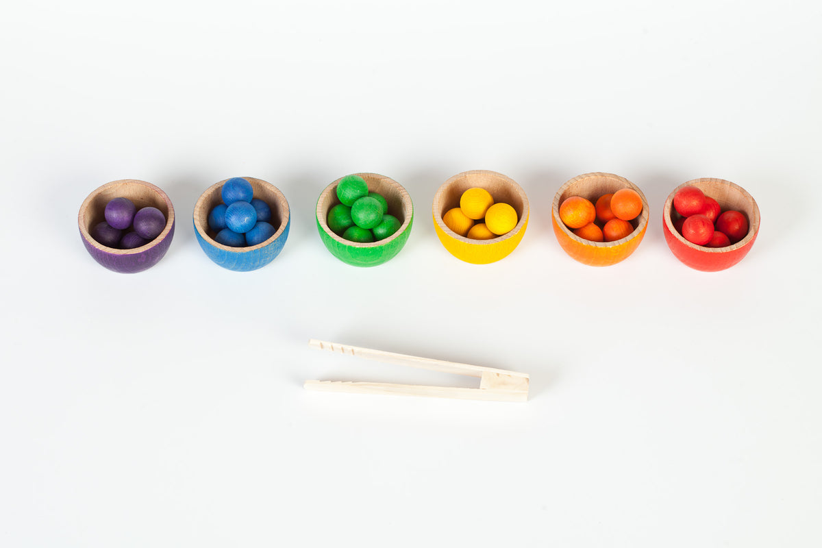 Colourful wooden toy bowls and colourful marbles with a pair of wooden tweezers 