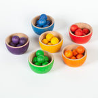 Set of colorful wooden toy bowls with small colourful wooden balls on a white background