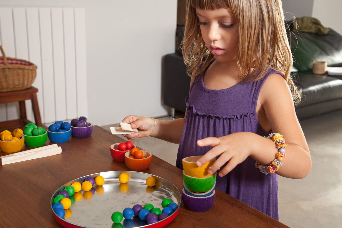 Child picking up colourful wooden marbles with a pair of tweezers and placing them in colourful wooden bowls