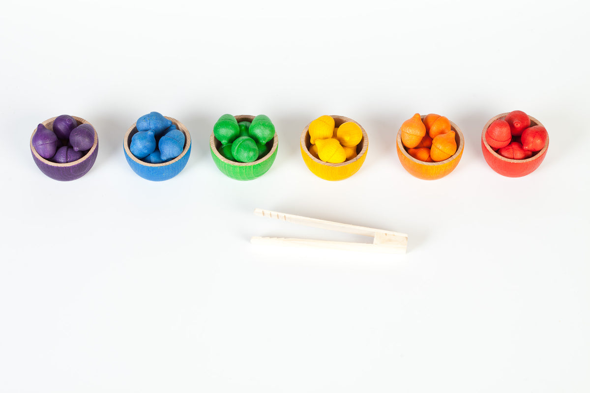 Set of colourful wooden toy bowls filled with wooden acorns and a pair of wooden tweezers 