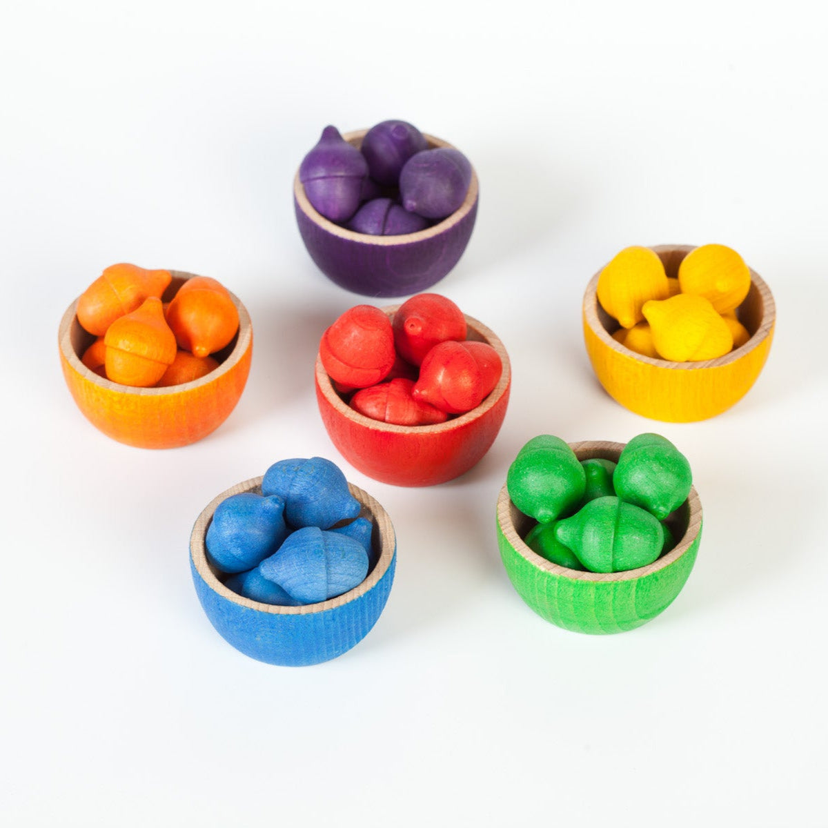 Set of colorful wooden toy bowls containing colourful wooden acorns on a white background