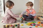 Two children playing with colourful wooden toys.  Stacking them on small logs.