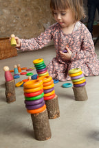 Child playing with colourful peg dolls, rings and discs on small logs